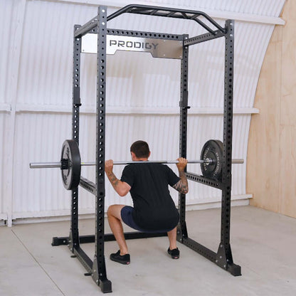 Man squatting inside the Prodigy Full Power Rack with weights, showcasing durable home gym equipment.